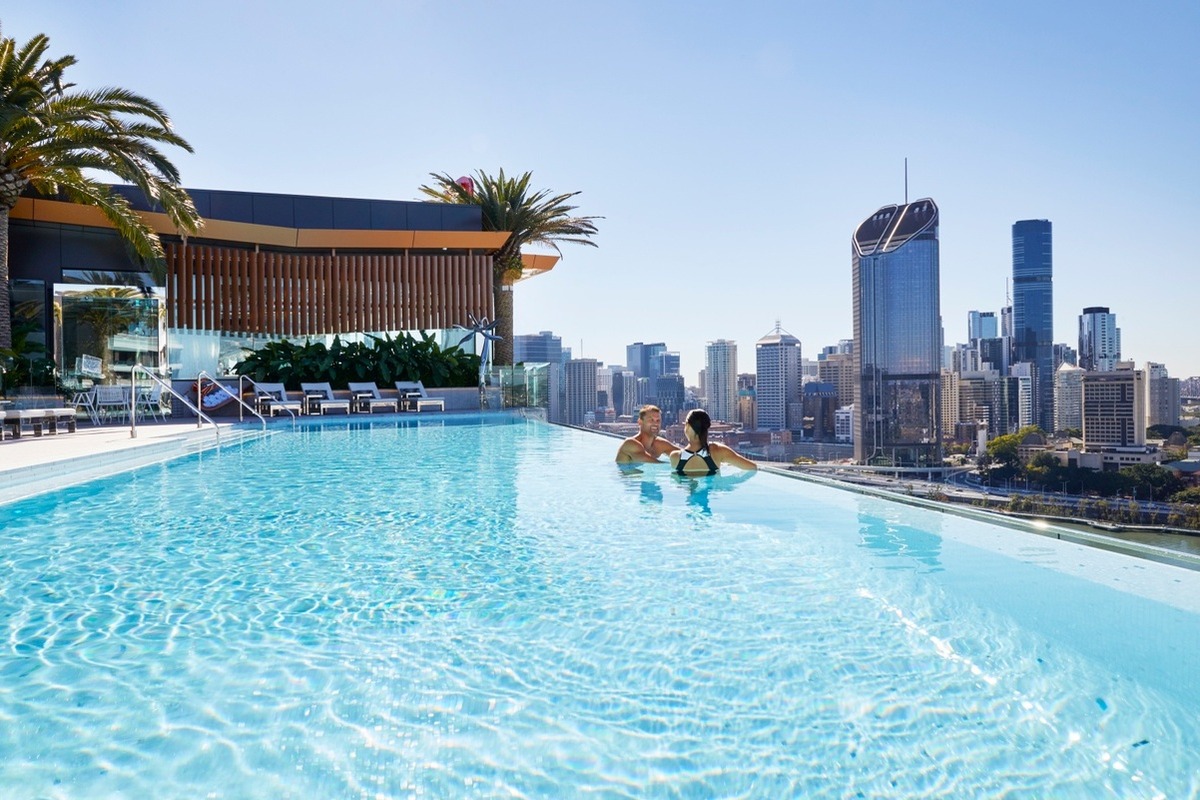 Image of young couple in the rooftop terrace infinity pool at The Emporium Hotel Southbank overlooking the Brisbane skyline